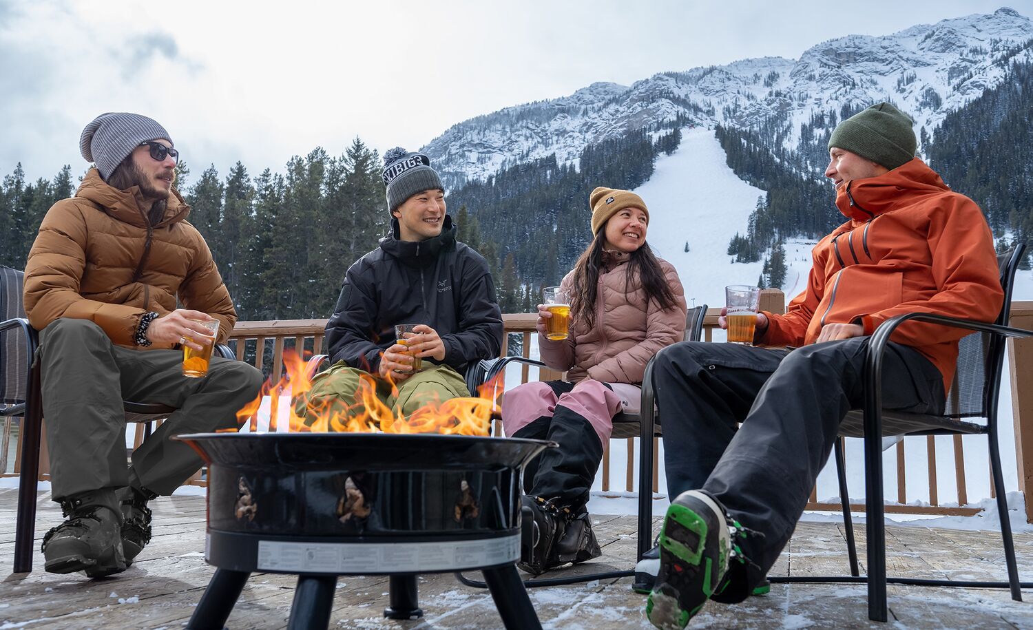 A group of friends enjoy a meal and drinks at an outdoor table at a Mt. Norquay with the ski hill in the background.
