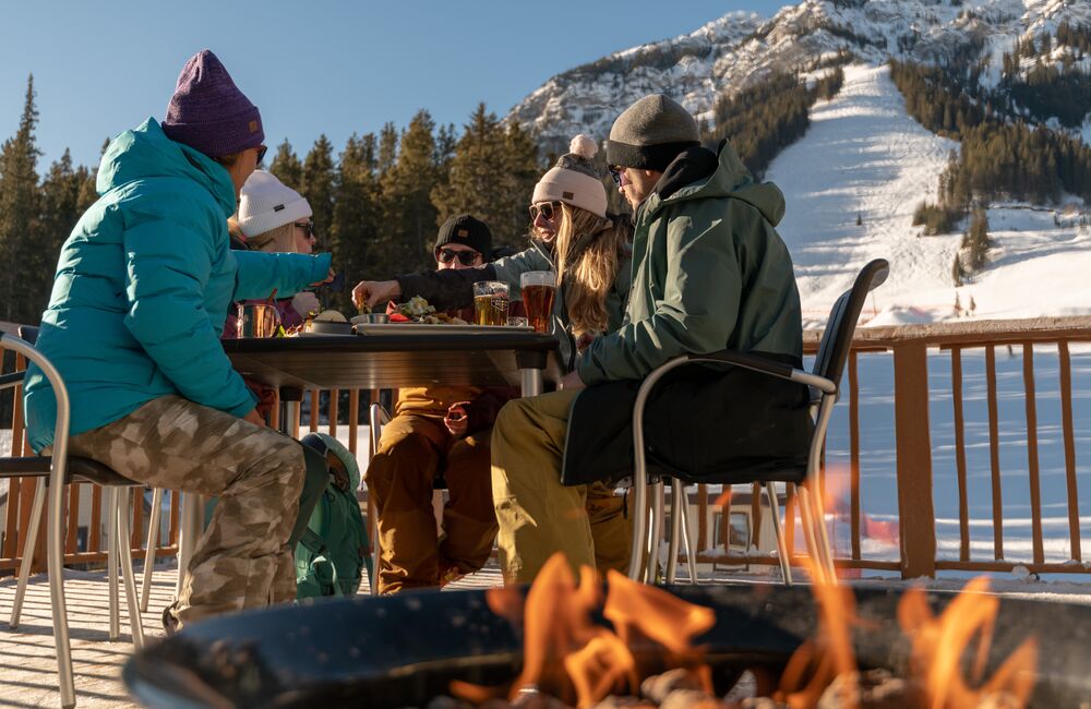 A group of friends enjoys food and drinks on a patio at Mt. Norquay ski resort in Banff National Park. 