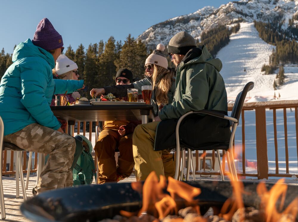 A group of friends enjoys food and drinks on a patio at Mt. Norquay ski resort in Banff National Park. 