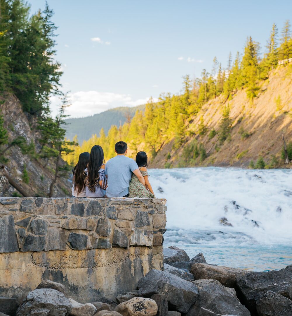 Family of 4 sitting on a wall looking at Bow Falls in Banff National Park