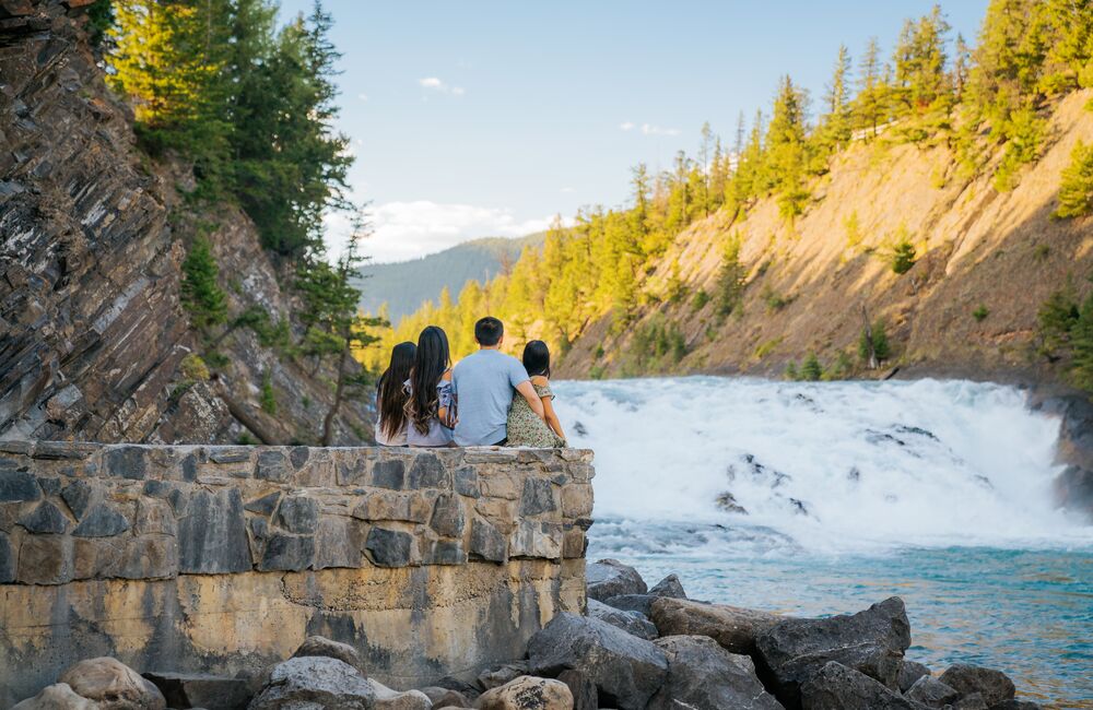 Family of 4 sitting on a wall looking at Bow Falls in Banff National Park