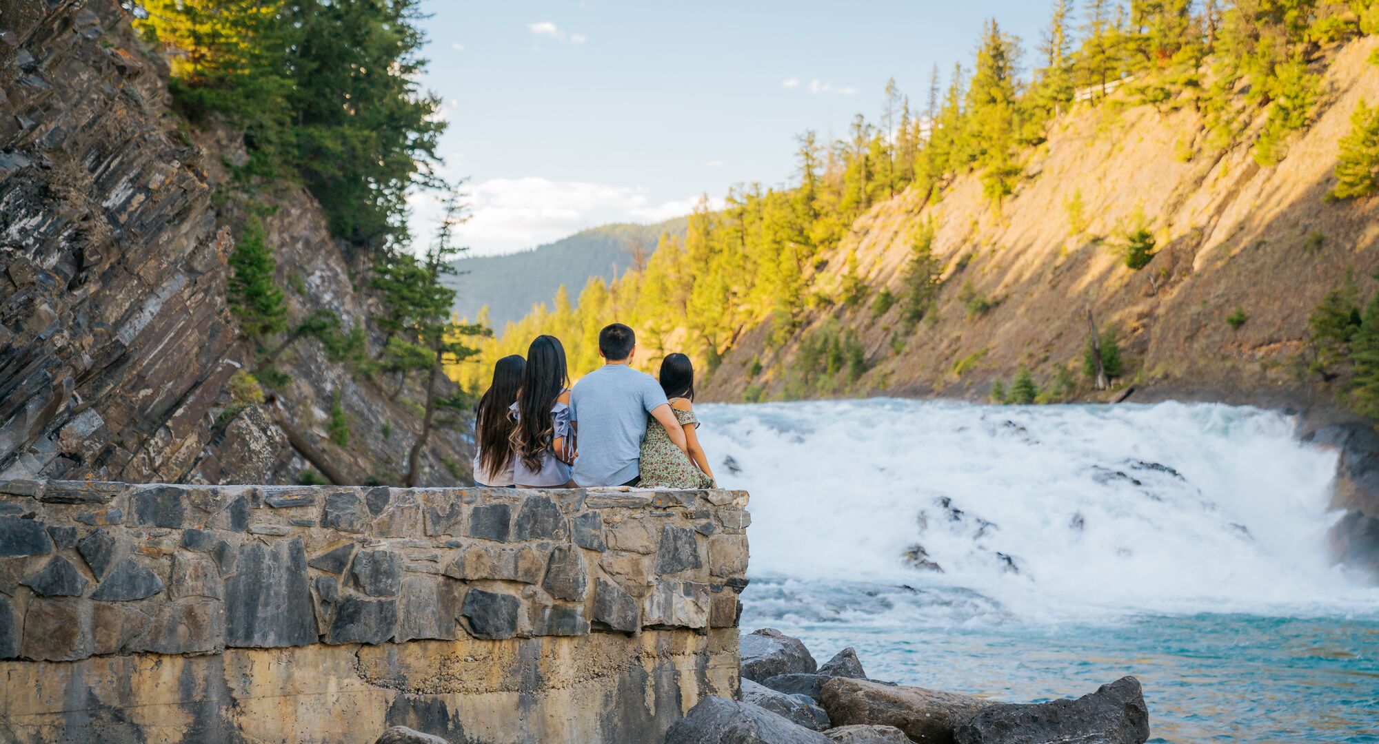 Family of 4 sitting on a wall looking at Bow Falls in Banff National Park