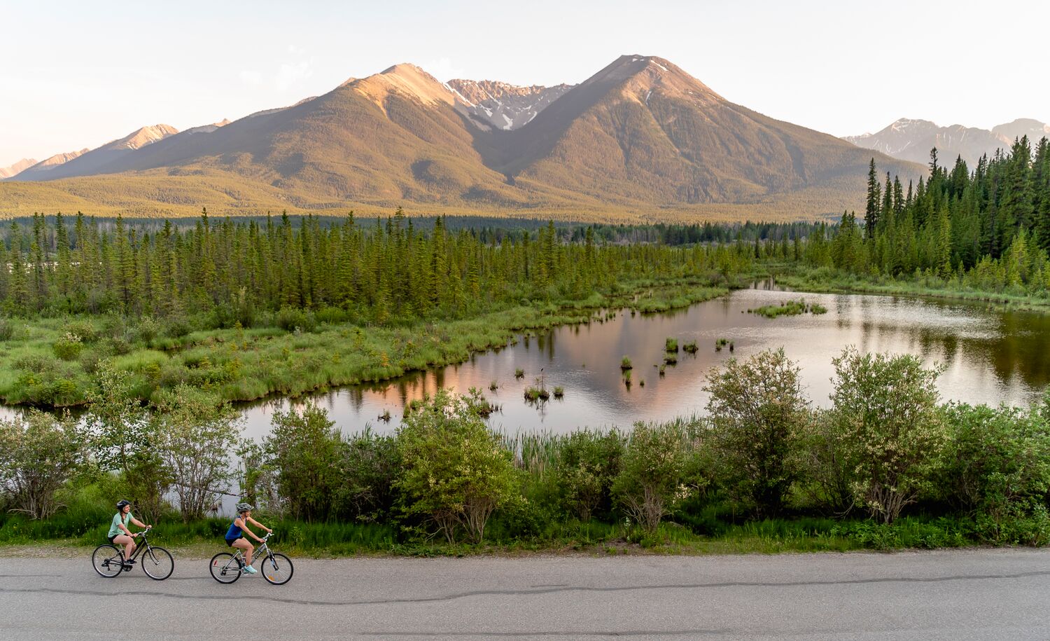 Two people bike beside Vermilion Lakes in Banff National Park.