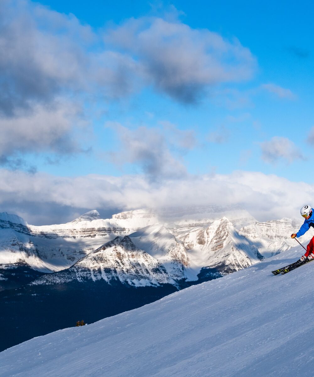 A skier on a run at the Lake Louise Ski Resort with mountains in the background in the winter.
