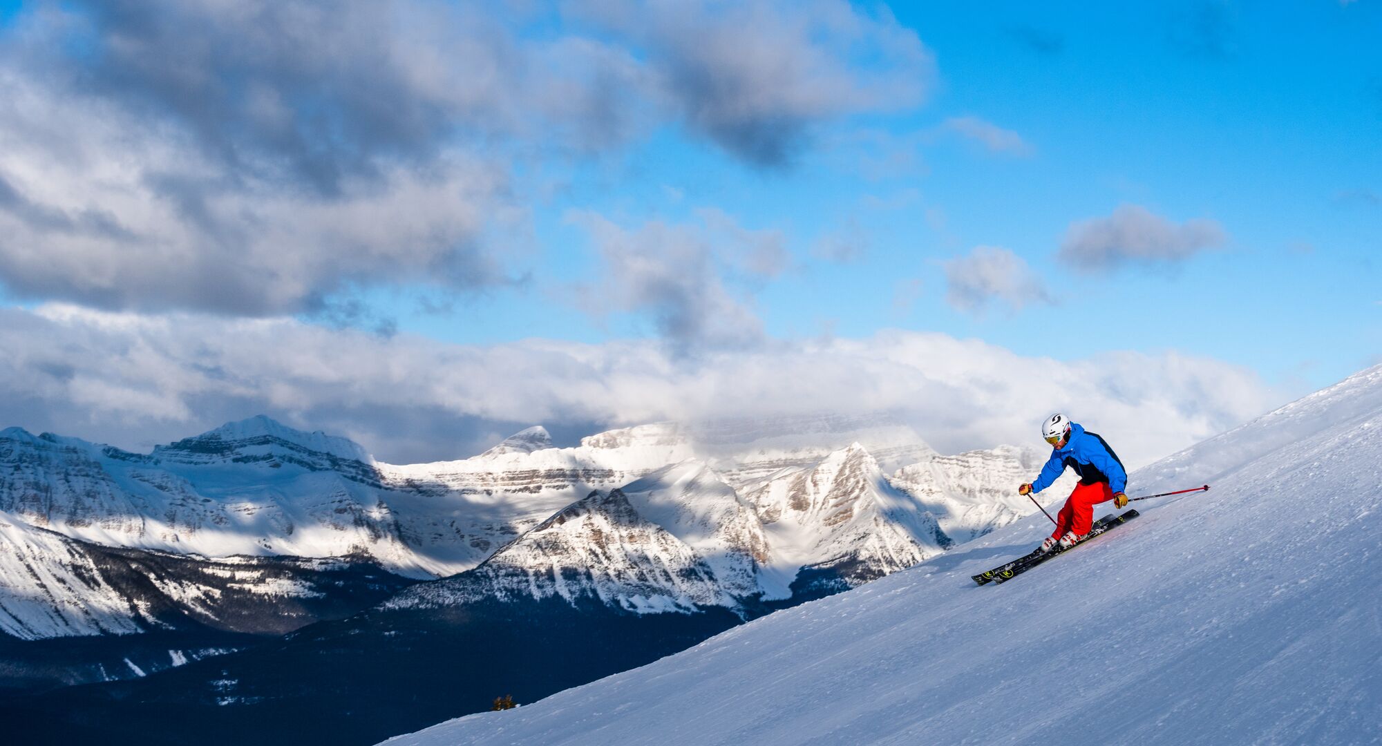 A skier on a run at the Lake Louise Ski Resort with mountains in the background in the winter.