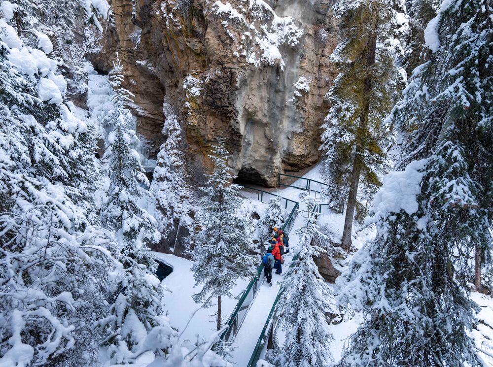 A tour group stands on a snowy bridge at Johnston Canyon Lower Falls as seen from above in Banff National Park.