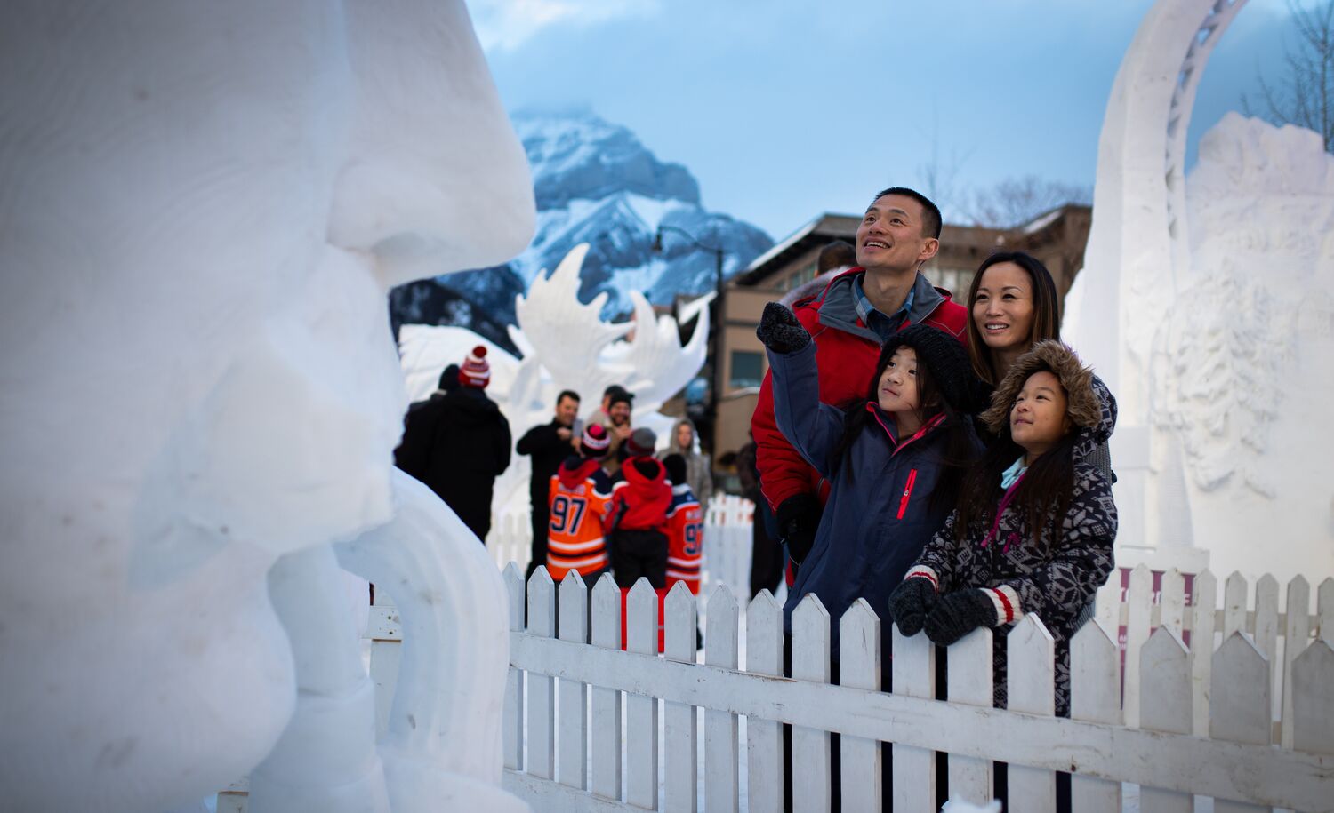 Family of four taking in the snow sculptures during SnowDays on Bear Street in Banff