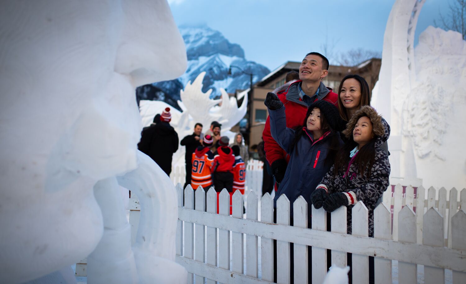 Family of four taking in the snow sculptures during SnowDays on Bear Street in Banff