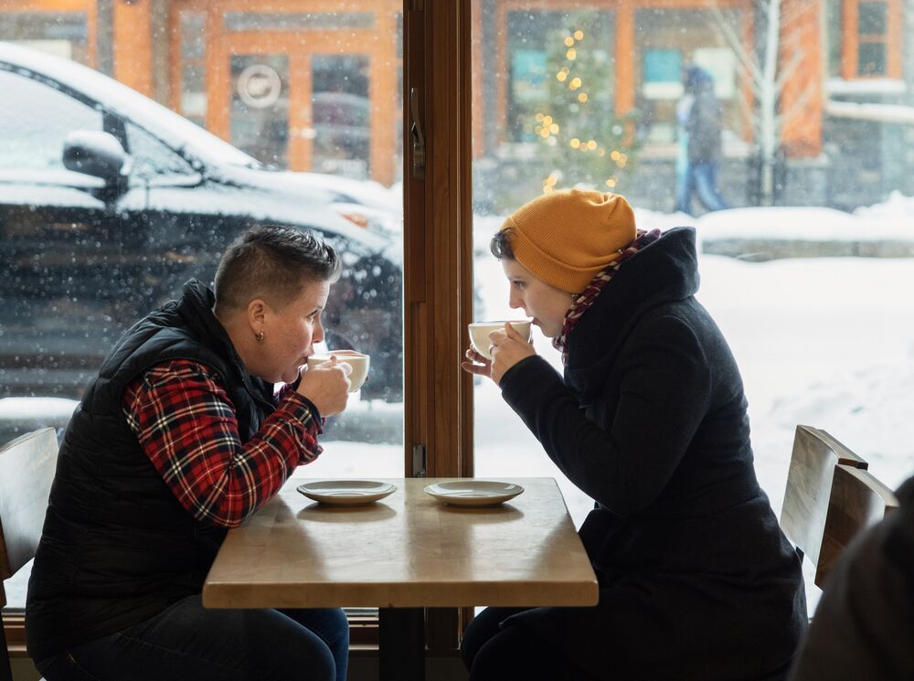 Two women sit by a window in Wild Flour in the winter drinking hot chocolate in Banff.