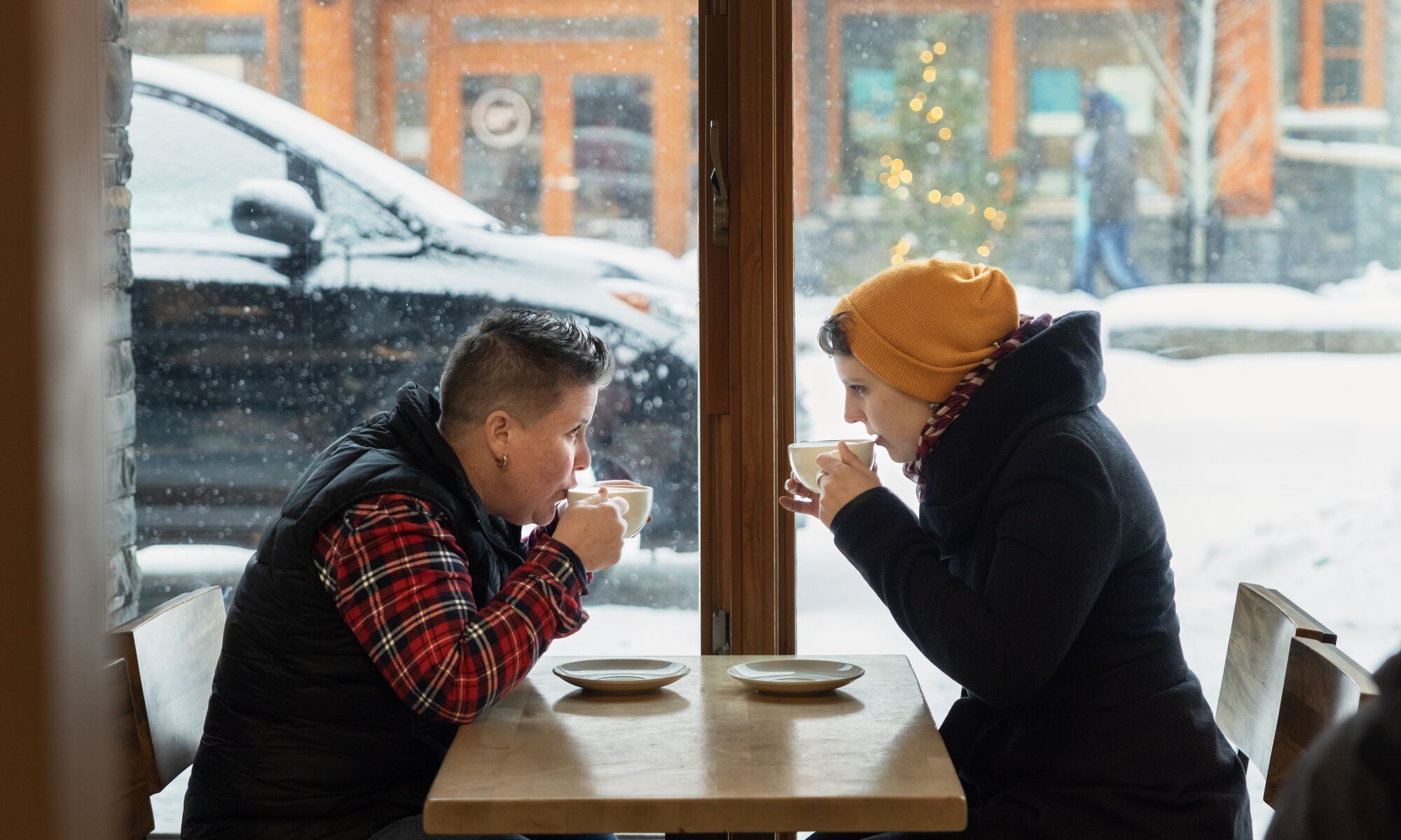 Two women sit by a window in Wild Flour in the winter drinking hot chocolate in Banff.