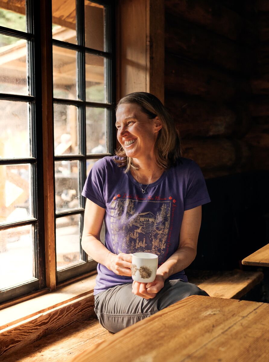 A person sits inside the Lake Agnes Tea House enjoying a hot drink while looking out the window at the views