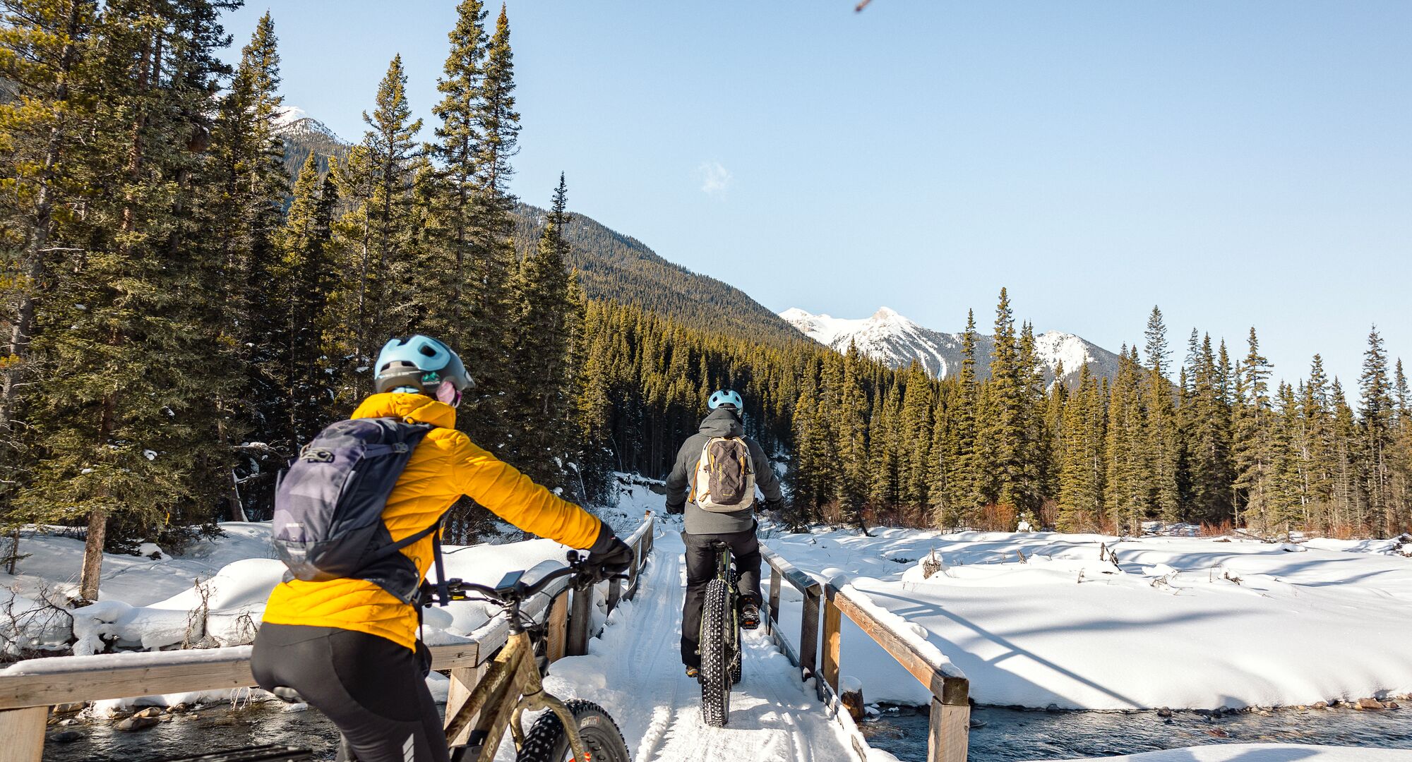 Two people fat tire biking across a bridge in Banff National Park in the winter