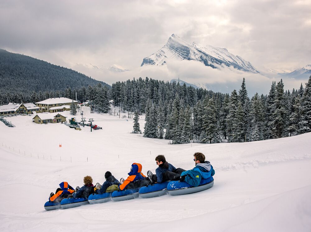 A group of people go tubing at Mt. Norquay in Banff National Park with Mount Rundle high in the background.