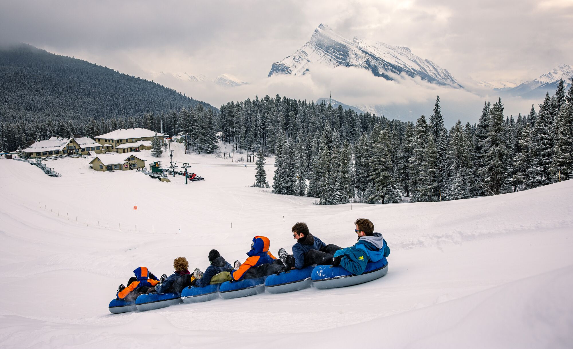 A group of people go tubing at Mt. Norquay in Banff National Park with Mount Rundle high in the background.