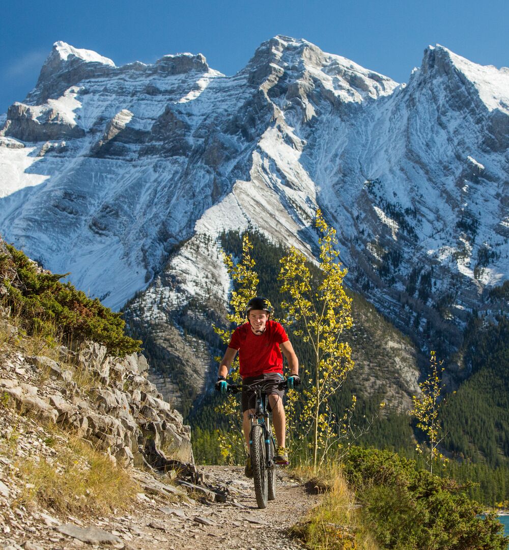 Person mountain biking the Lake Minnewanka trail with mountains and a lake in the background