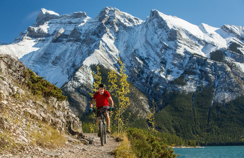 Person mountain biking the Lake Minnewanka trail with mountains and a lake in the background