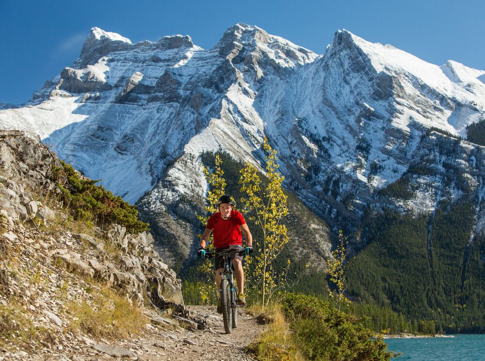Person mountain biking on the Minnewanka Trail with the lake and mountains in the background
