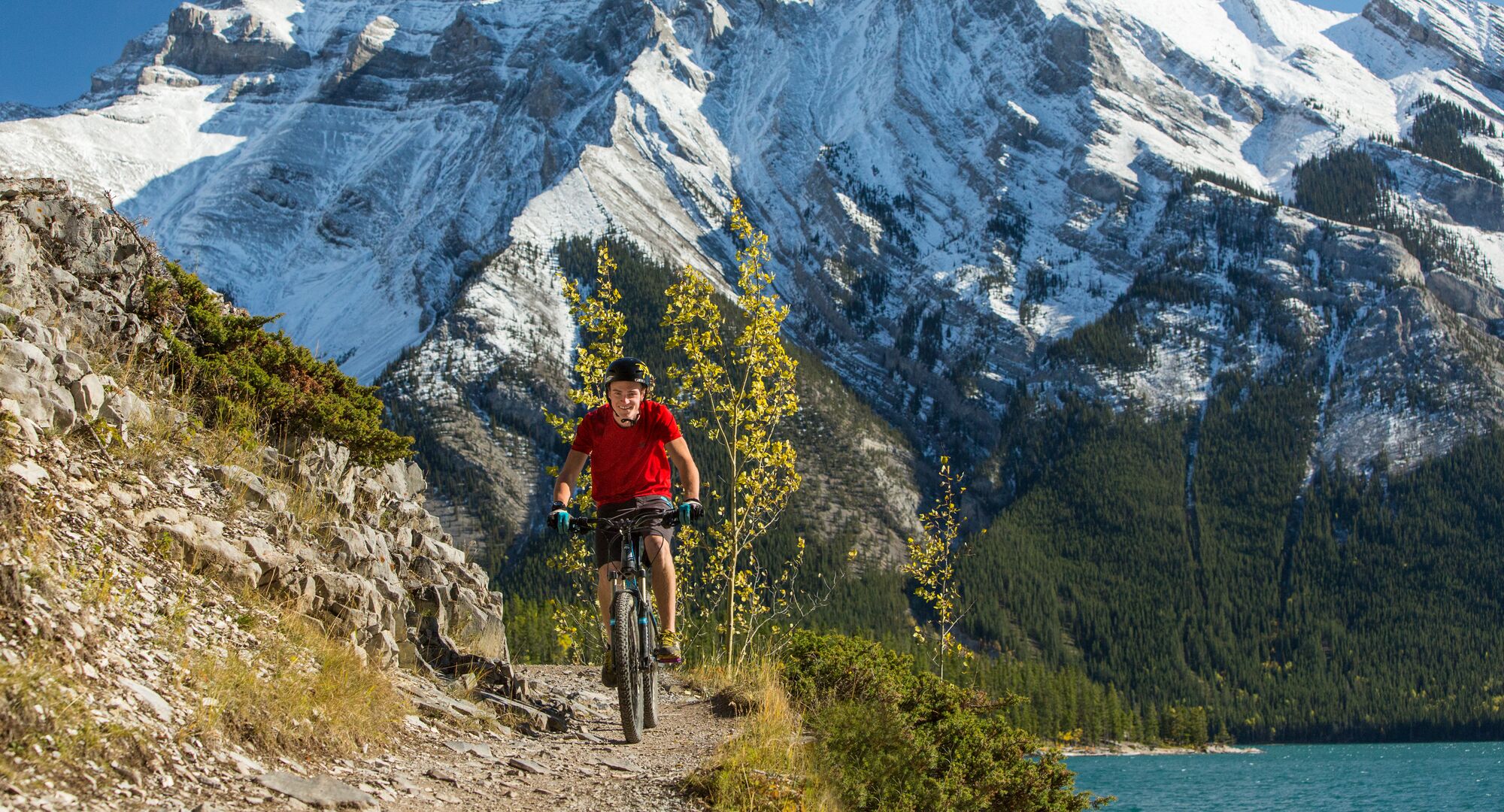 Person mountain biking on the Minnewanka Trail with the lake and mountains in the background