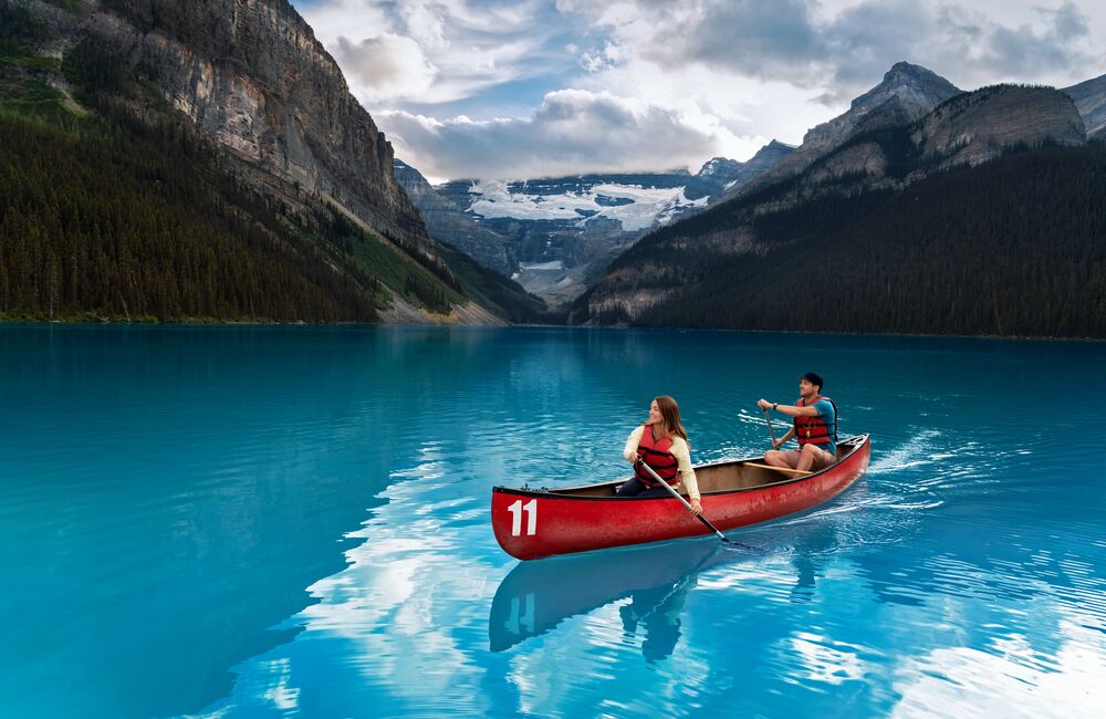 Two people paddling a red canoe on a summer day on Lake Louise in Banff National Park.