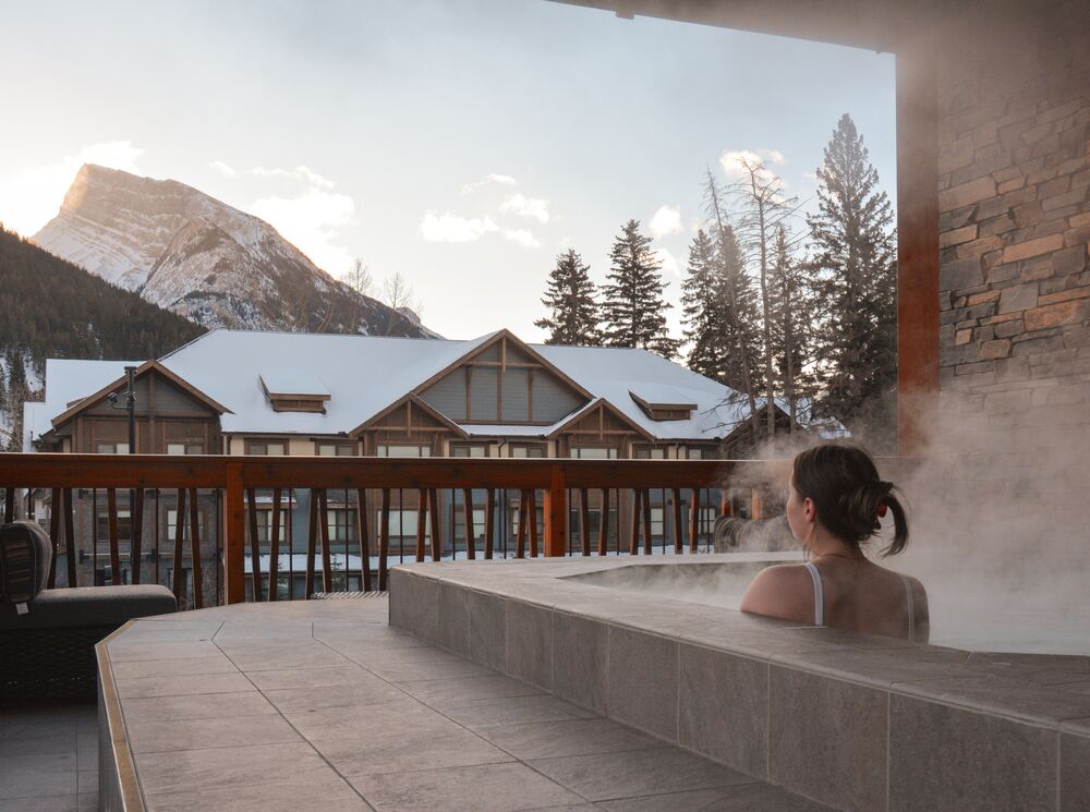 A woman sits in a rooftop hot tub at the Moose Hotel looking at Mount Rundle in Banff.