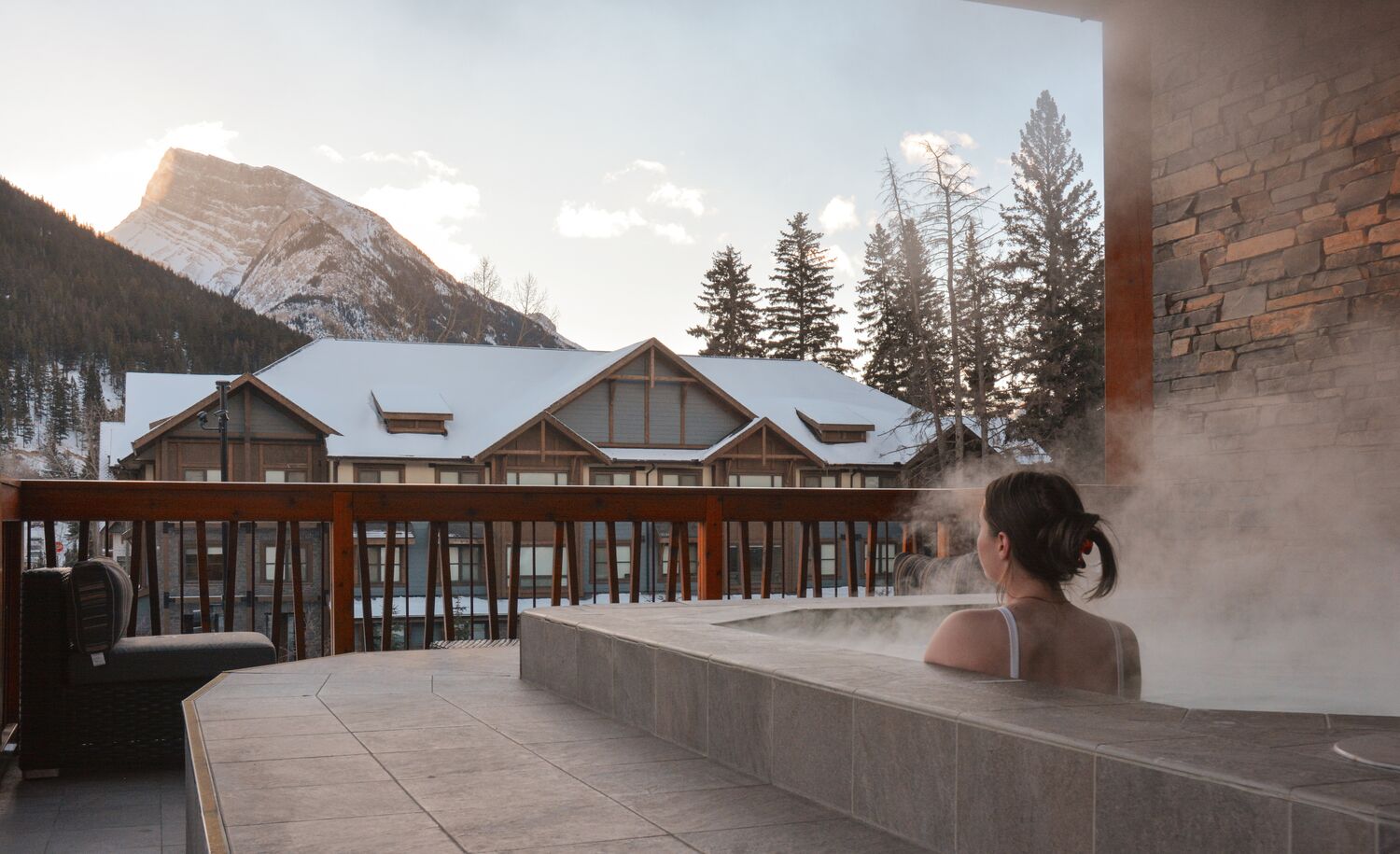 A woman sits in a rooftop hot tub at the Moose Hotel looking at Mount Rundle in Banff.