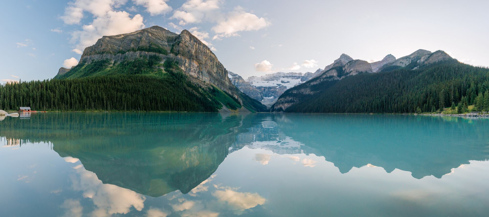 A view of turquoise Lake Louise from the shoreline on a summer day at sunset.