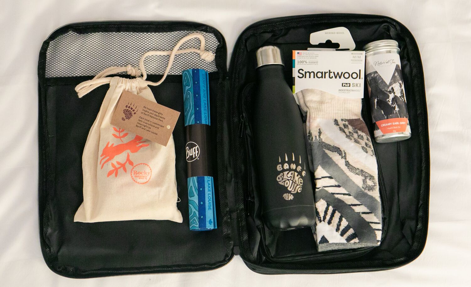 Suitcase with souvenirs from Banff: Water bottle, Smartwool socks, Rocky Mountain Soap, a Buff, and local tea.