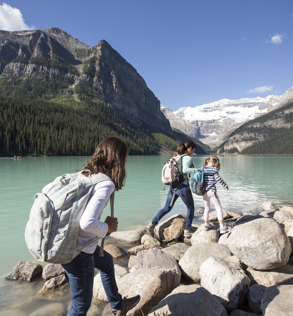 A family hiking along the shoreline of Lake Louise in the summer