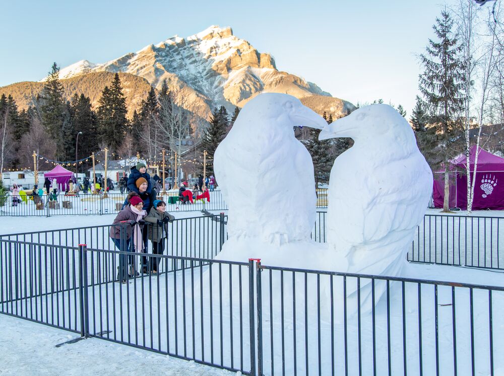 A family looks at a life-sized snow sculpture with Cascade Mountain in the background in Banff National Park.