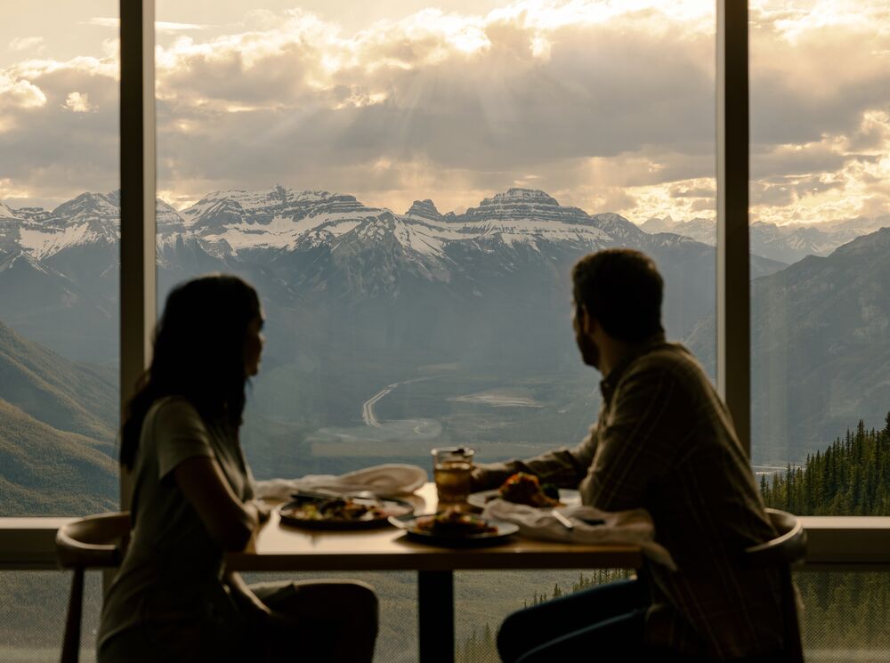 Two people eating looking at the views at Sky Bistro in Banff National Park.