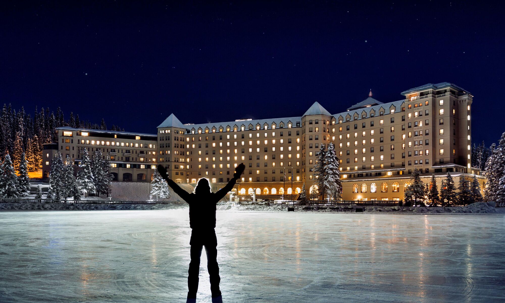 Photo of a man enjoying the view of the Fairmont Chateau Lake Louise in Banff National Park on a winter night.