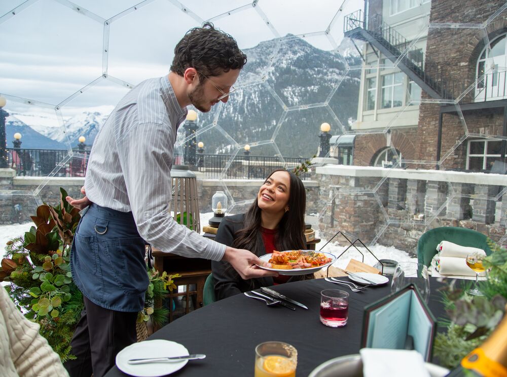 A woman receives a plate of food from a waiter in a transparent 360 dome at the Fairmont Banff Springs Hotel in Banff, Canada.