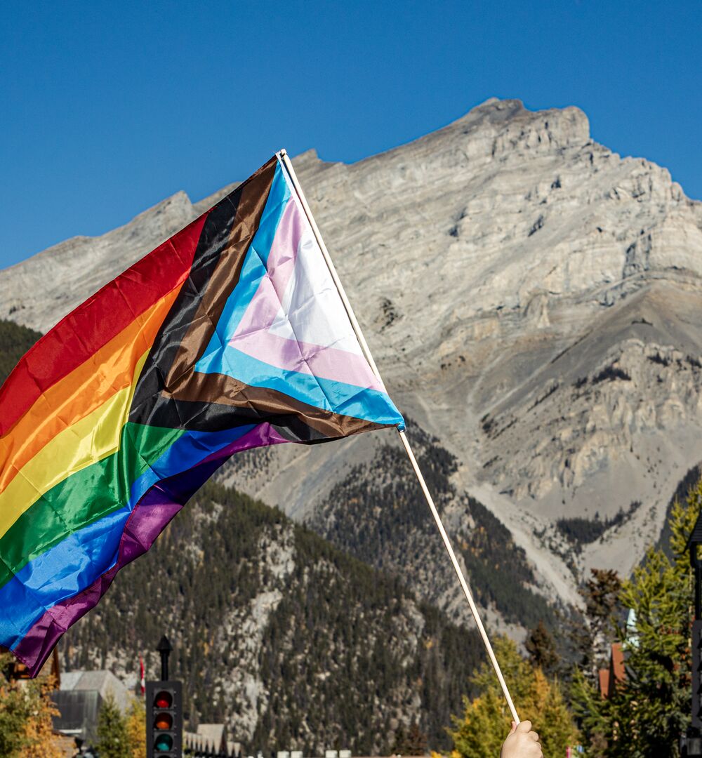 A pride flag waves in the air in front of Cascade Mountain on Banff Ave in Banff National Park.