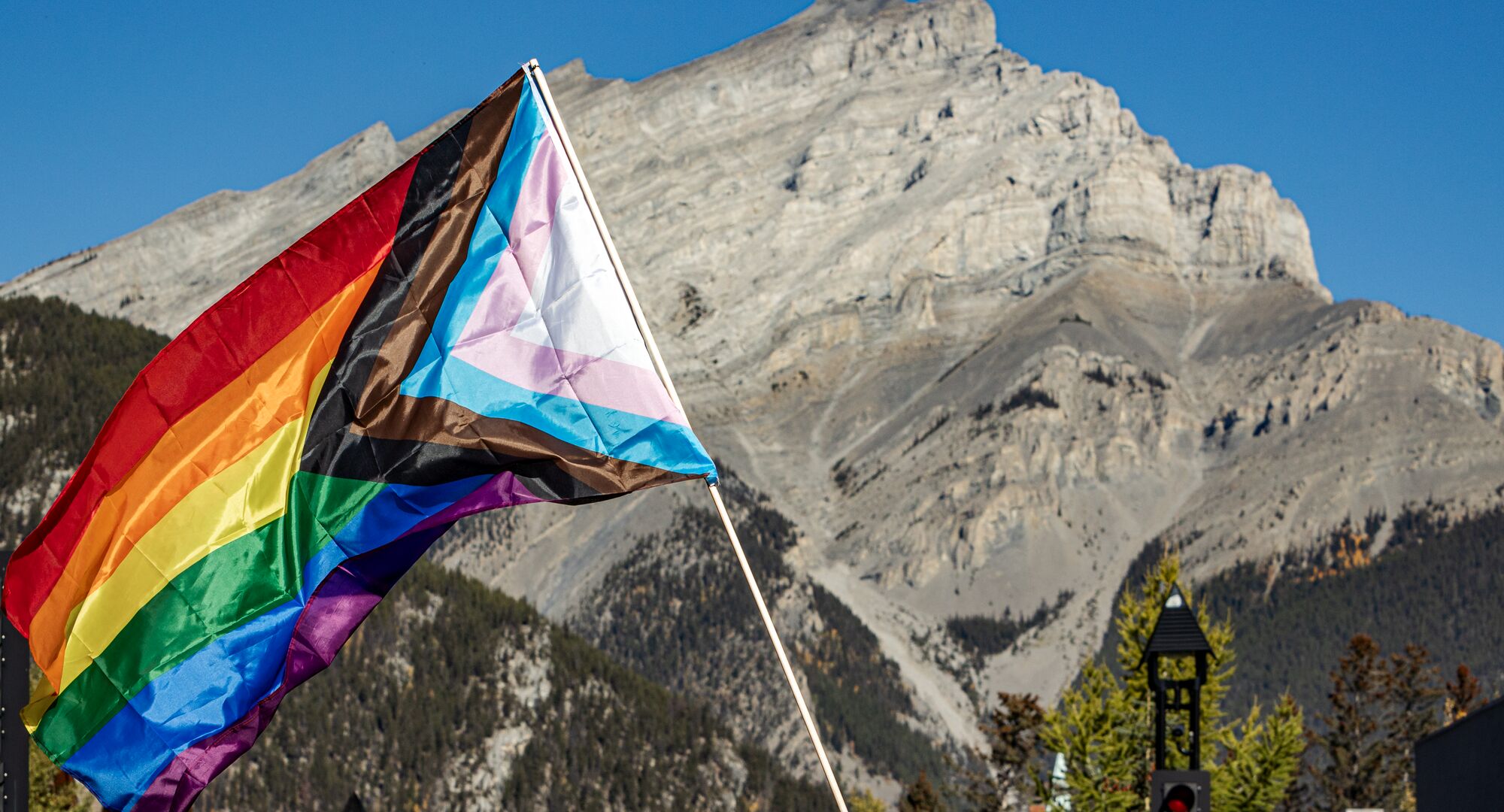 A pride flag waves in the air in front of Cascade Mountain on Banff Ave in Banff National Park.