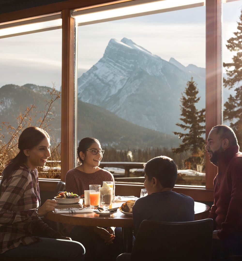 A family of four enjoy a meal at the Juniper Bistro with a view of Mount Rundle out the window