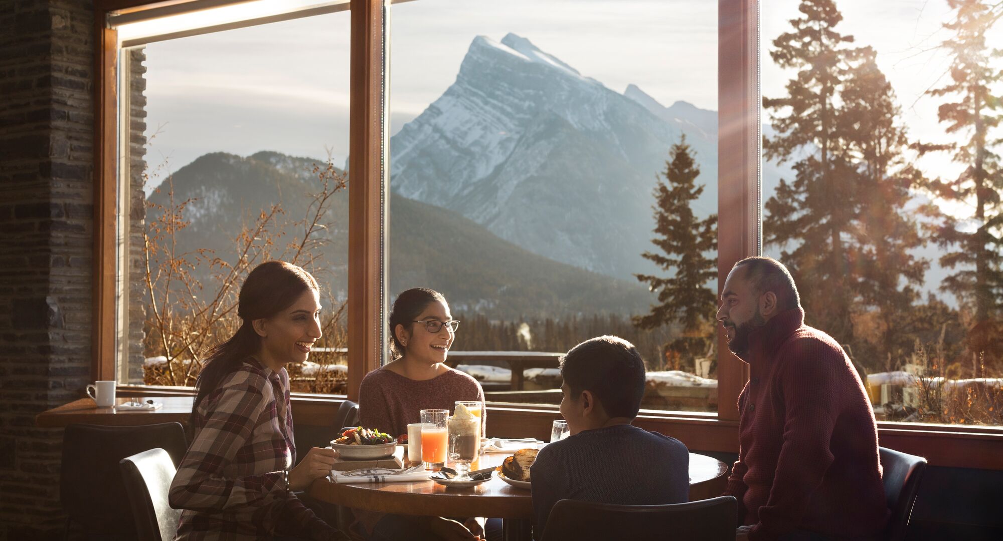 A family of four enjoy a meal at the Juniper Bistro with a view of Mount Rundle out the window