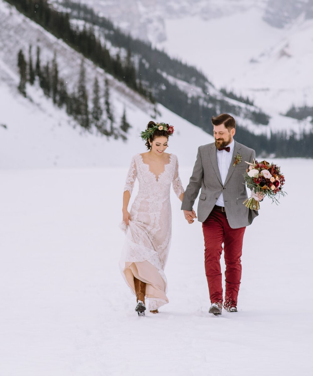 A bride and groom walk through the snow at Lake Louise on their wedding day