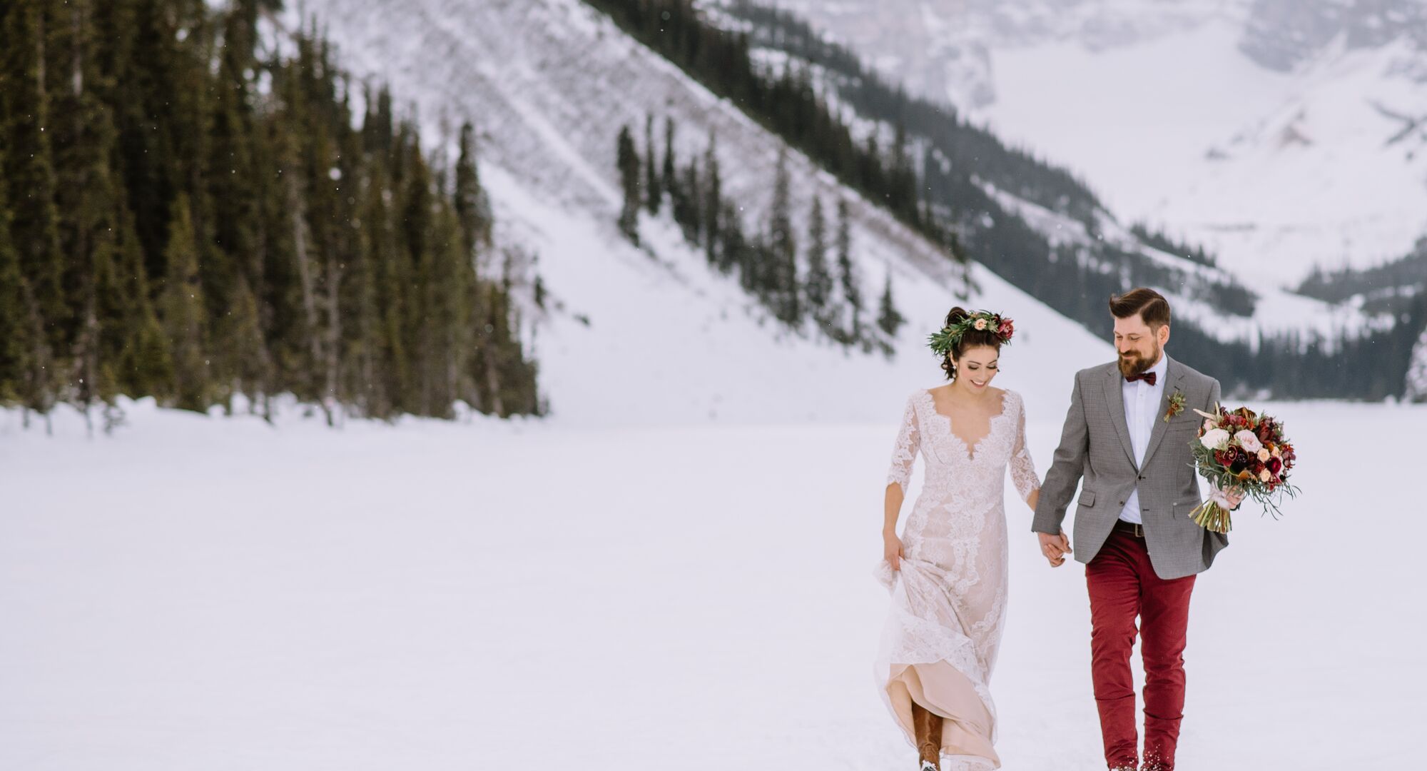 A bride and groom walk through the snow at Lake Louise on their wedding day