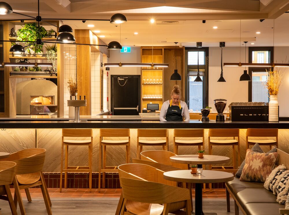 Interior photo of wooden chairs and tables and a server at a bar in Farm & Fire in Banff.