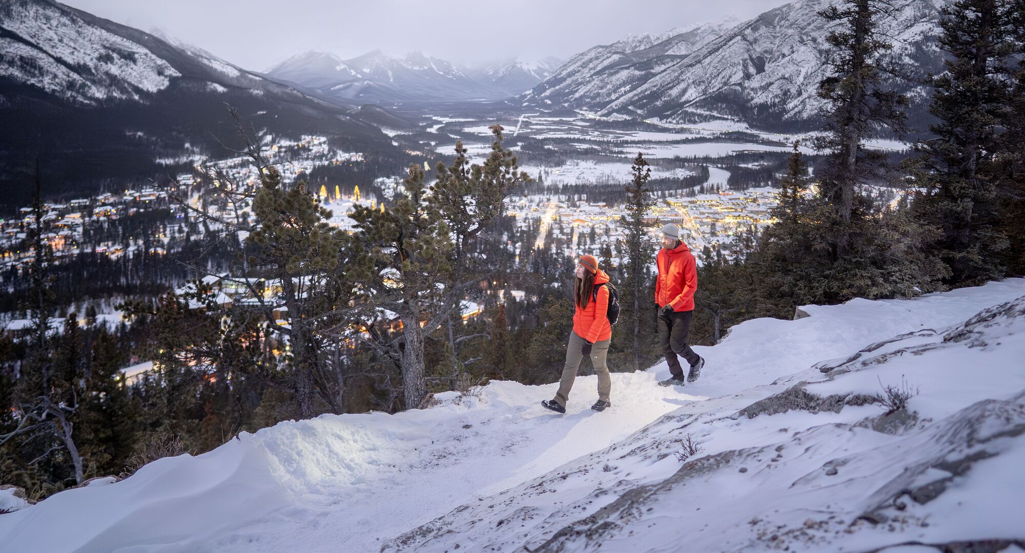 Two people hiking the Tunnel Mountain trail in the winter with views looking back over Banff town.