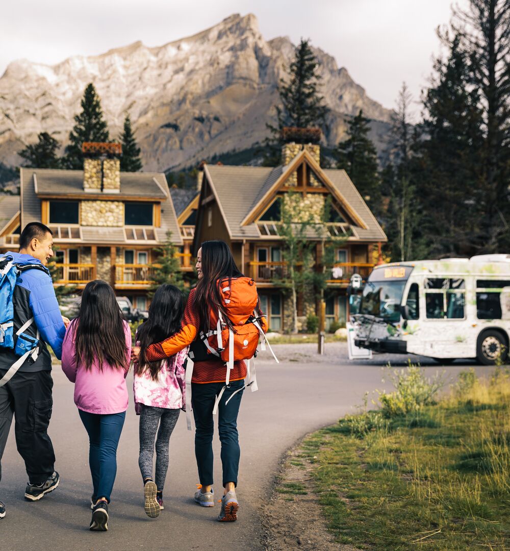 A family walks towards a Roam Transit bus at Tunnel Mountain Resort in Banff National Park.