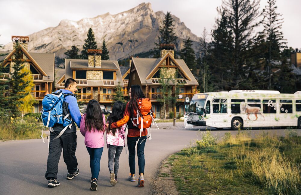 A family walks towards a Roam Transit bus at Tunnel Mountain Resort in Banff National Park.