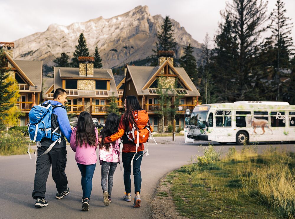 A family walks towards a Roam Transit bus at Tunnel Mountain Resort in Banff National Park.