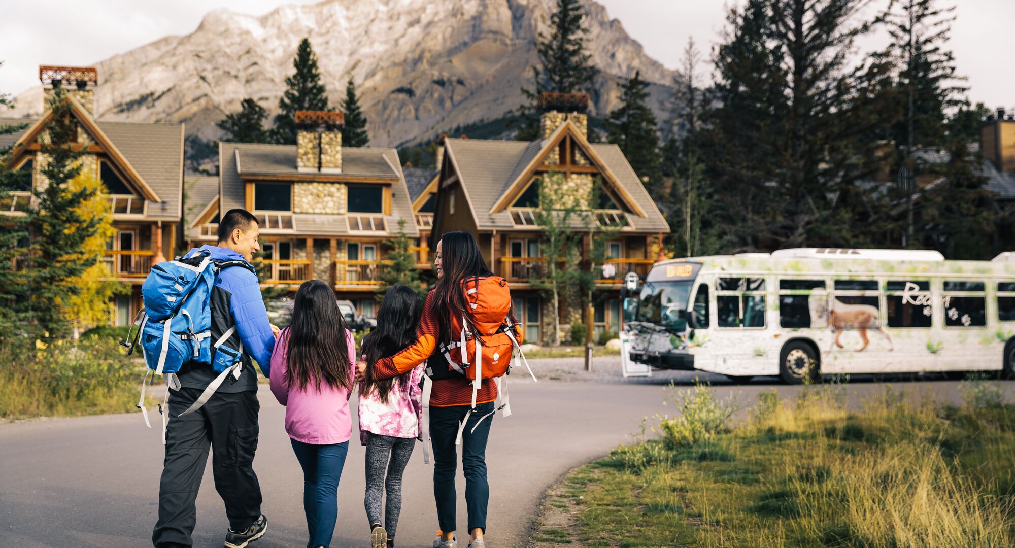 A family walks towards a Roam Transit bus at Tunnel Mountain Resort in Banff National Park.