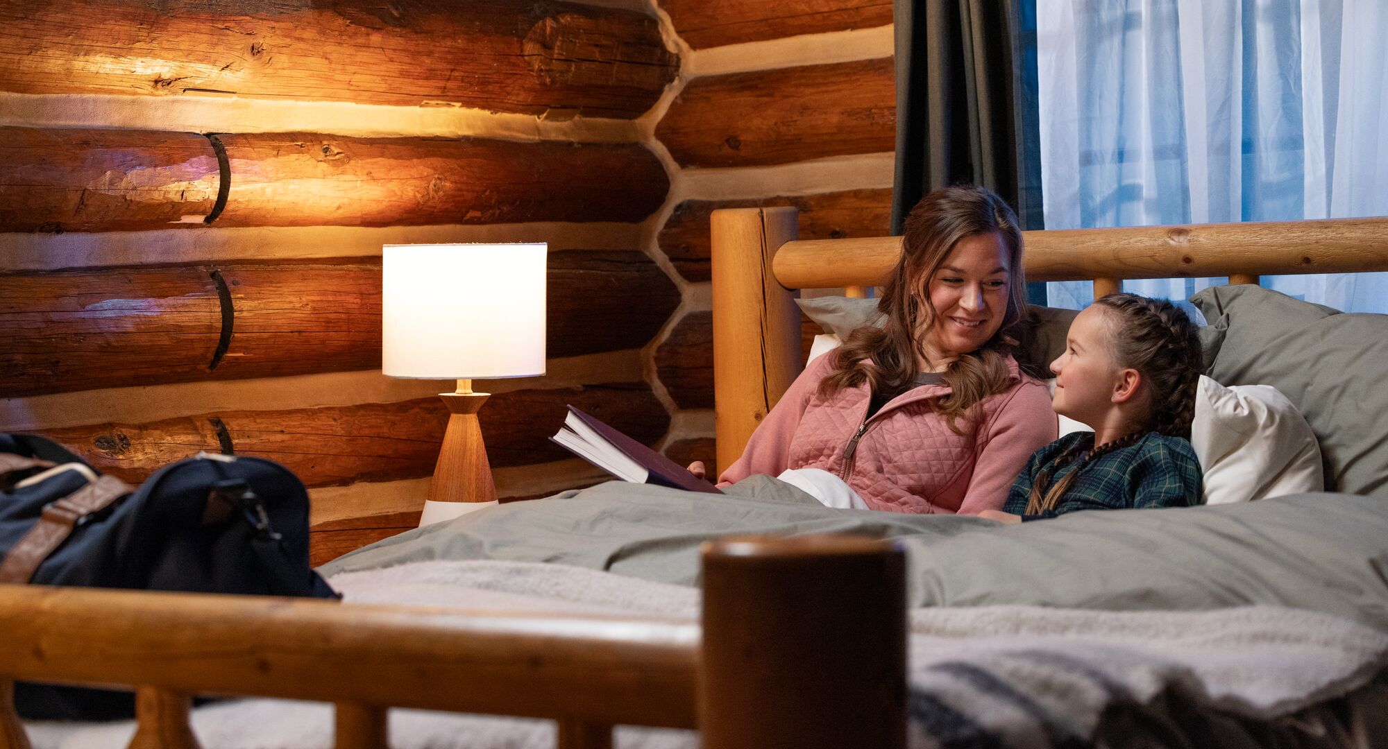 A mother and daughter reading a story on a bed in Storm Mountain Lodge in Banff National Park.
