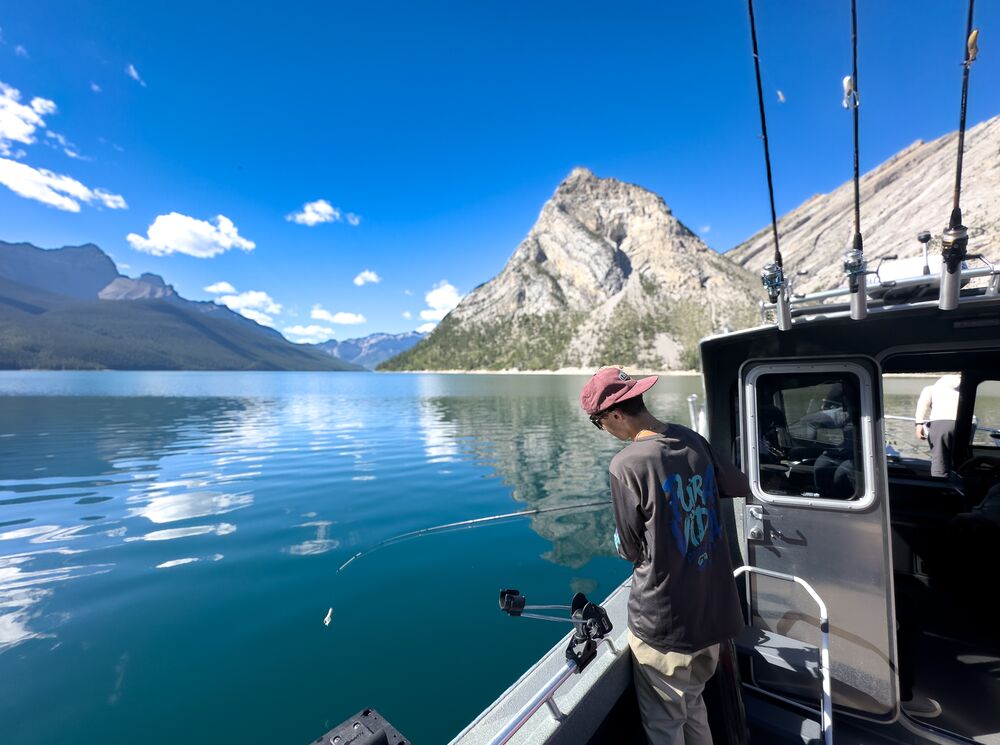 A person fishing on a boat in Lake Minnewanka, a popular thing to do in Banff in July