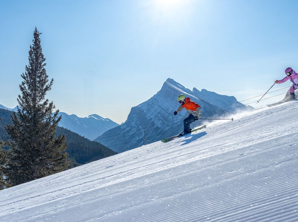 Two skiers enjoying the freshly groomed trails at Mount Norquay near Banff on a sunny winter day.