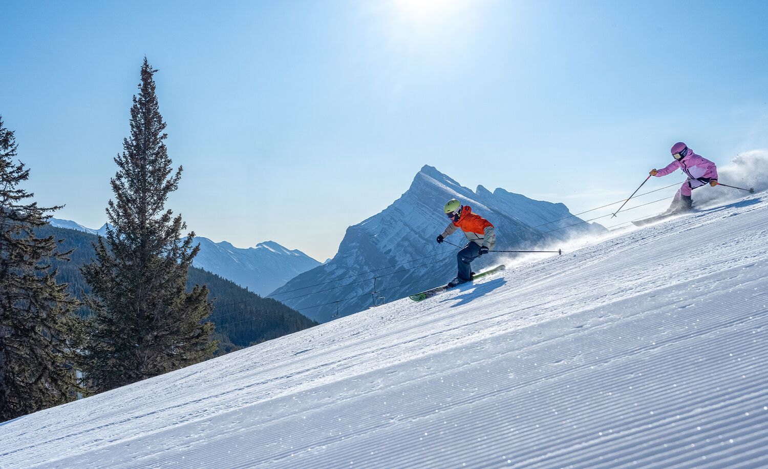 Two skiers enjoying the freshly groomed trails at Mount Norquay near Banff on a sunny winter day.