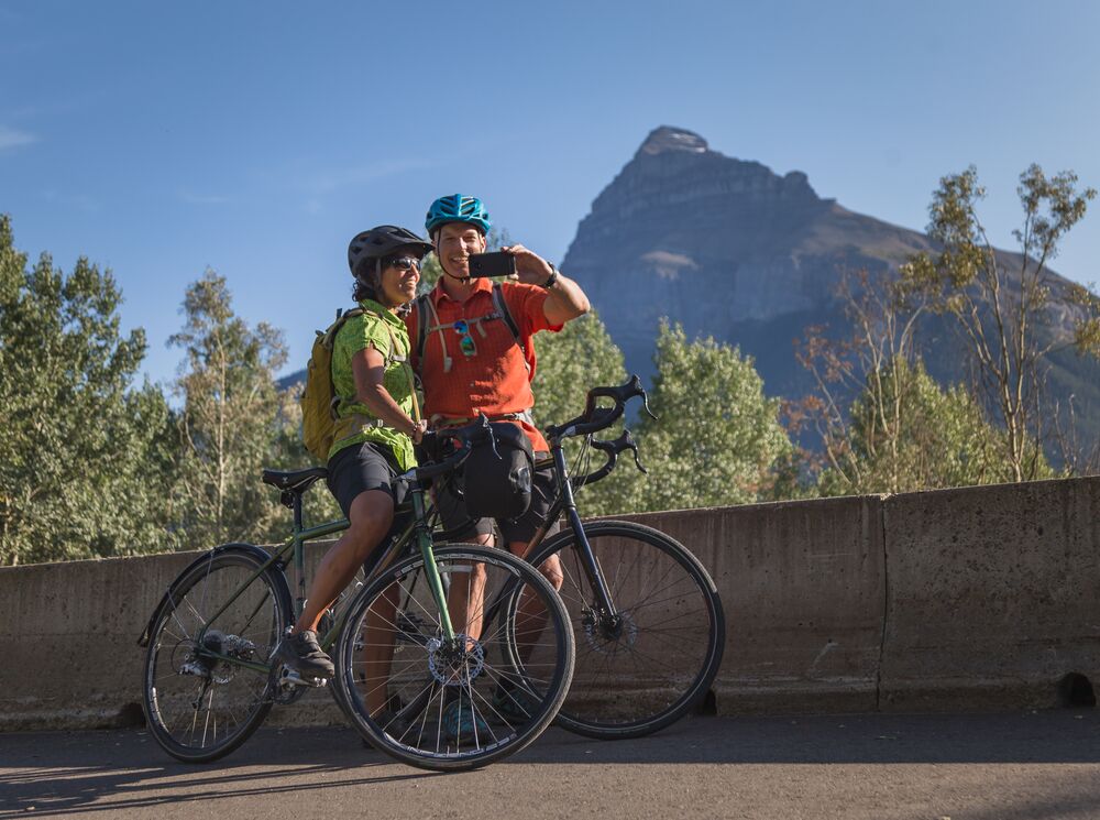 Two cyclists take a selfie while stopped on the Bow Valley Parkway in the summer.