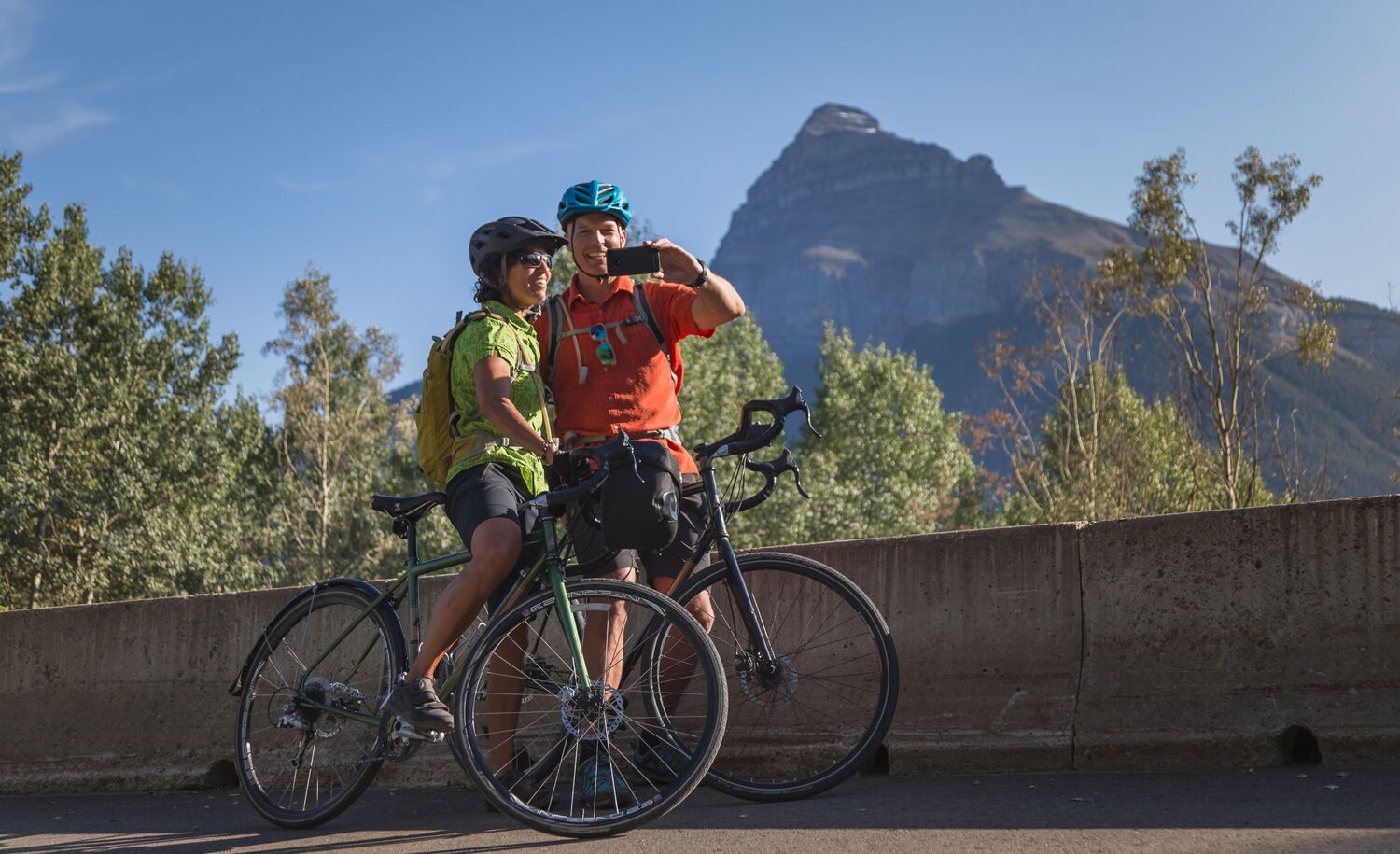 Two cyclists take a selfie while stopped on the Bow Valley Parkway in the summer.